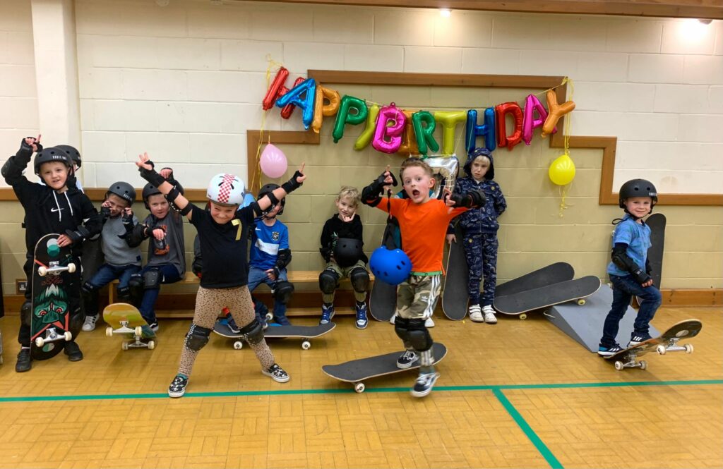 Birthday parties at The Skate Club. Group of children with skateboarding gear and a happy birthday banner.